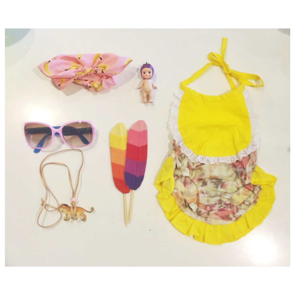 flatlay showing kids items of a yellow bathing suit, feathers, sunglasses, headband and sonny angel frm moppit thelotco former retail business