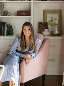 woman with long brown hair wearing a blue dress and murkani silver jewellery (kiralee mcnamara) sitting on chair in living room with books behind her on shelf.