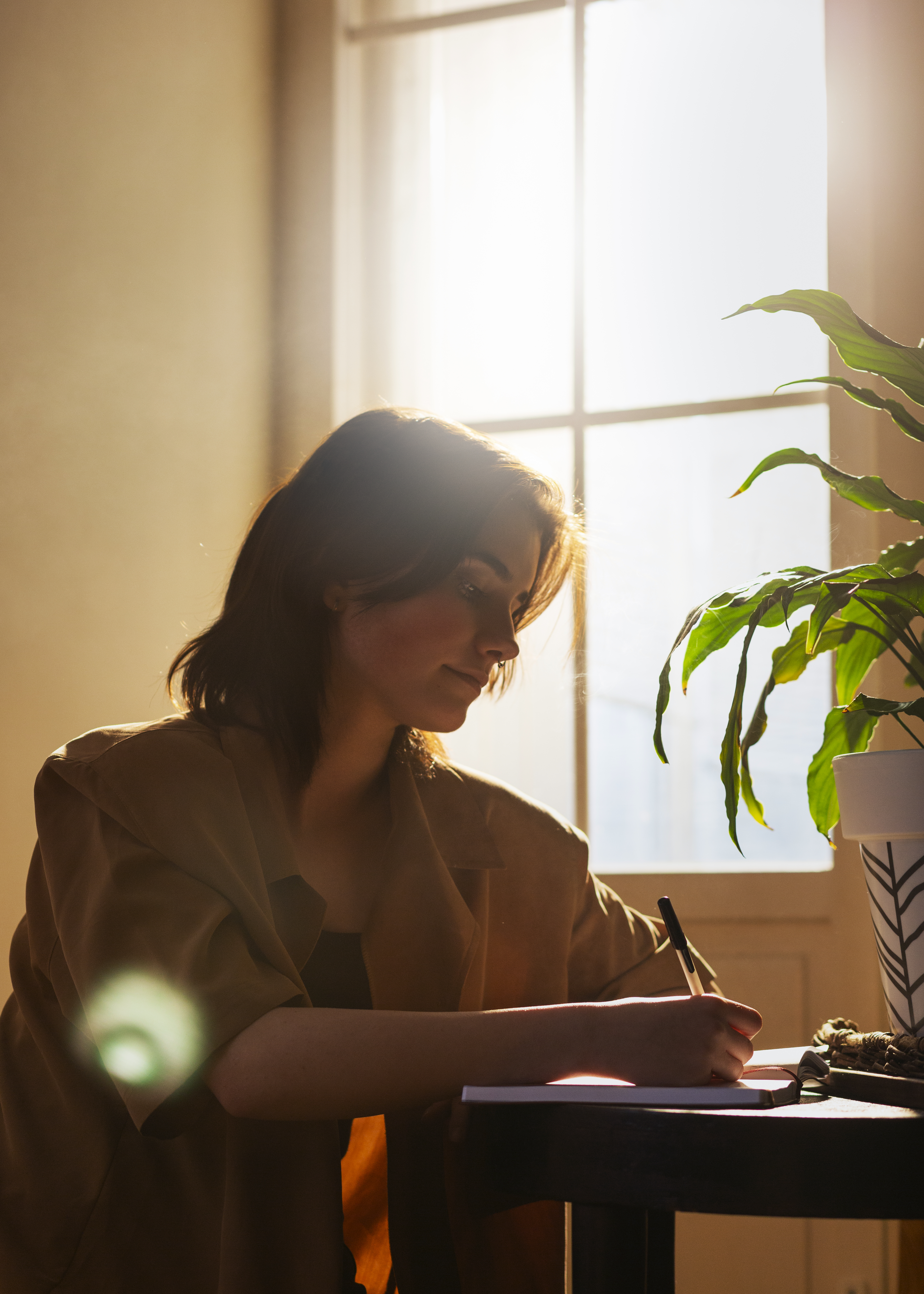 short haired woman writing beside the window with sun shines